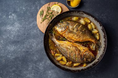 Koyu arkaplanda soğan ve otlarla pişirilmiş deniz mahsulü veya dorada..