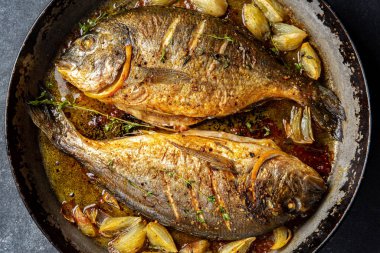Koyu arkaplanda soğan ve otlarla pişirilmiş deniz mahsulü veya dorada..
