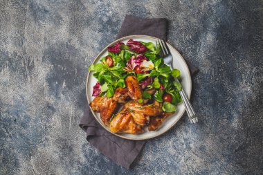 Kızarmış bbq kanatları ve domatesli yeşil salata. Üst görünüm.