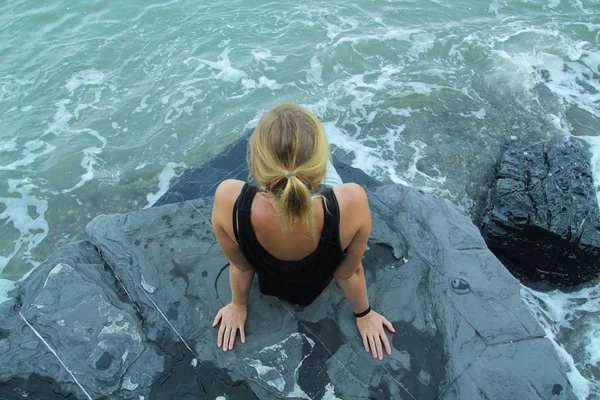 Outdoor woman alone sitting on stone coast and looking at sea