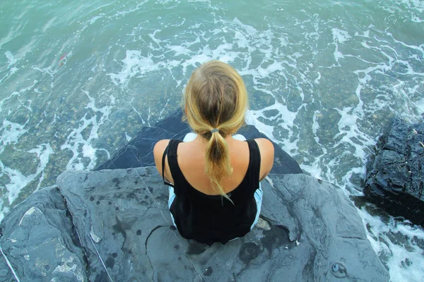 Mulher ao ar livre sozinho sentado na costa de pedra e olhando para o mar — Fotografia de Stock