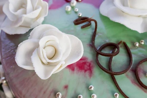 Bleken van een roos uit de glazuur op de bruidstaart tegen de achtergrond van chocolade en groen-roze glazuur — Stockfoto