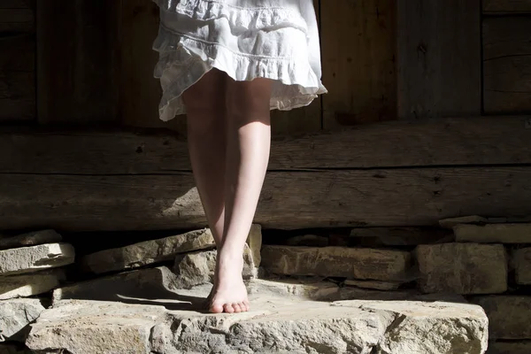 Eski taş basamaklarda yalın ayak duran beyaz elbiseli bir kızın bacakları. — Stok fotoğraf