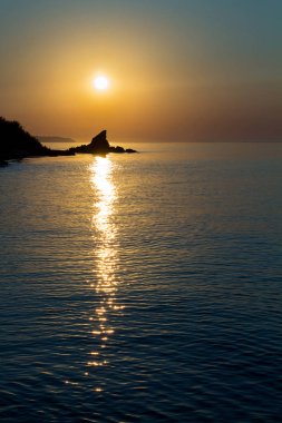 Denizde gün doğumu, okyanus, bir uçurumun arka planında, aynı dikey çizgide güneşten parlayan bir uçurum, sıcak ve soğuk renklerde fotoğraf