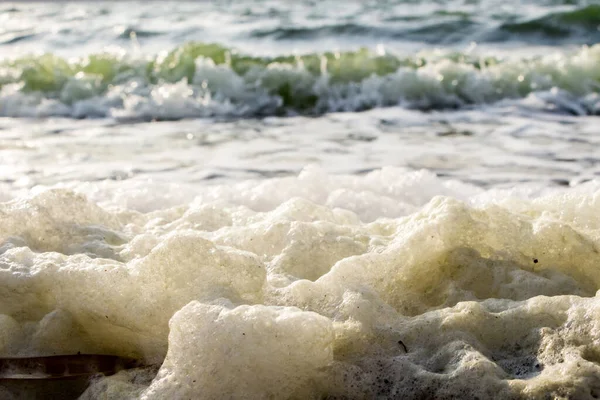 Poluição ambiental, close-up sujo de espuma amarela jogado pelas ondas na praia — Fotografia de Stock
