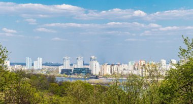 Kiev, Ukrayna 'nın sol kıyısındaki panorama, yüksek binalar, Dinyeper Nehri ve kıyı şeridindeki altyapı, ön plandaki ağaçlar, yaz, güneşli gün.