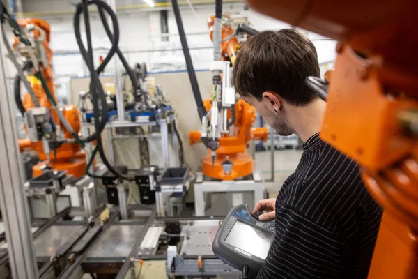 Молодой человек программирует промышленный автоматический робот в автомобильной промышленности — стоковое фото