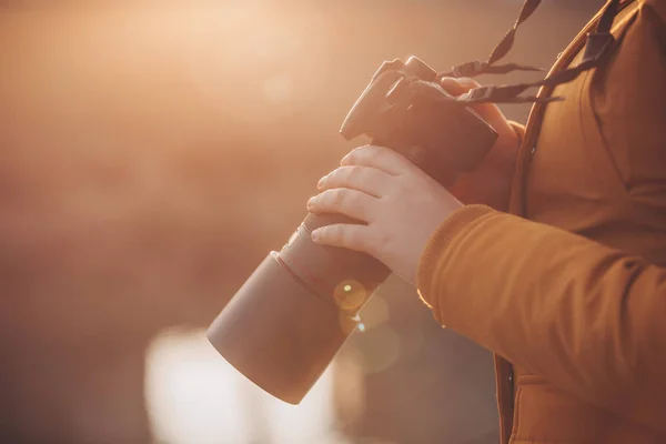 Ung kvinna, fotograf håller professionell camer i händerna under härlig solnedgång — Stockfoto