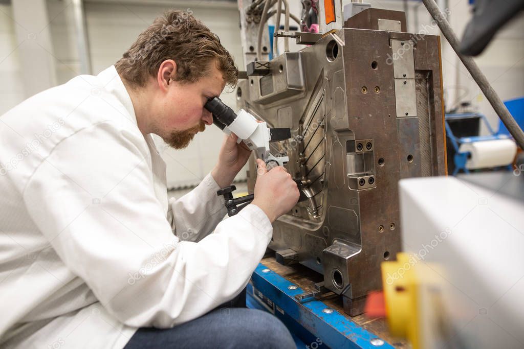 Quality engineer checks deficiencies on the injection mold by a microscope, industrial concept