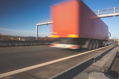 Otobanda geçiş kapısından geçen bir kamyon. Otoyol harcamaları, hareket bulanık.