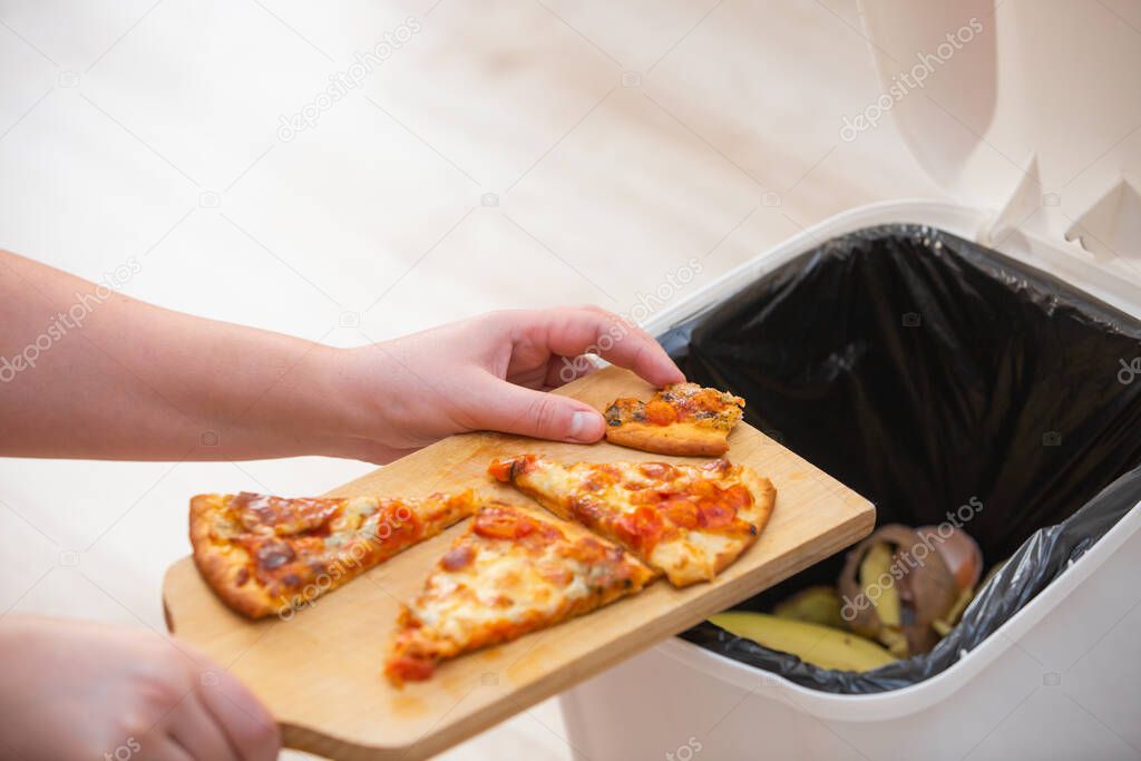 Stop wasting food, Woman hand throwing some food, pizza pieces to the bin, trash, food concept
