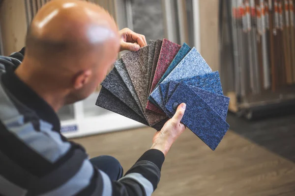 De man die de juiste kleur en het juiste materiaal van tapijt kiest voor zijn nieuwe appartement in de studio, en huishoudens inricht — Stockfoto