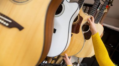 Bir kadın müzik aleti dükkanından yeni bir tahta gitar almaya çalışıyor, enstrümantal konsept.