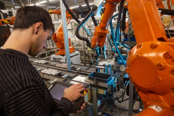 Repairman doing repair on automatic robot arms in huge automotive factory, industrial concept