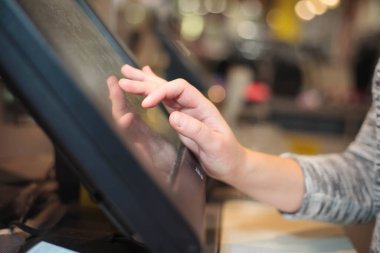 Genç bir kadın, büyük bir alışveriş merkezinde dokunmatik ekran hazinesi ve finans konseptiyle bazı giysiler için para alıyor.