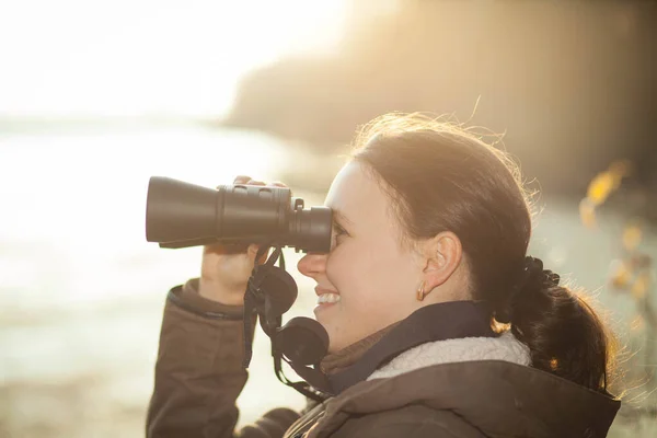 Ung brunett kvinna som tar hand om djuren genom professionella teleskop i naturreservat, ornitologi koncept — Stockfoto