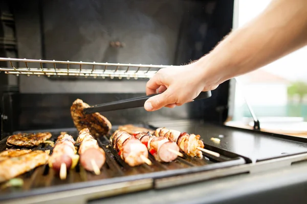 Junger Mann dreht Fleisch mit Gabel auf dem Gasgrill, Grillkonzept — Stockfoto