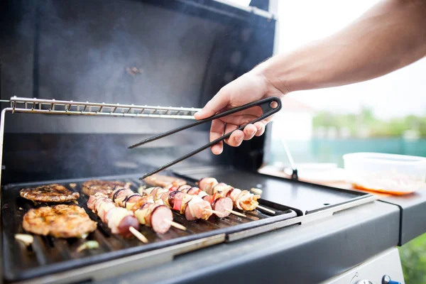 Hand eines jungen Mannes grillt Fleisch- und Gemüsespieße auf riesigem Gasgrill, Grillkonzept — Stockfoto