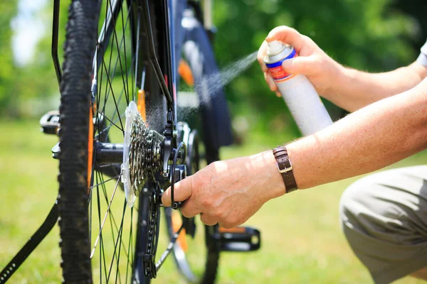 Senior man händer besprutning en olja till kedjan från hjulet cykeln, gör underhåll av sin cykel — Stockfoto