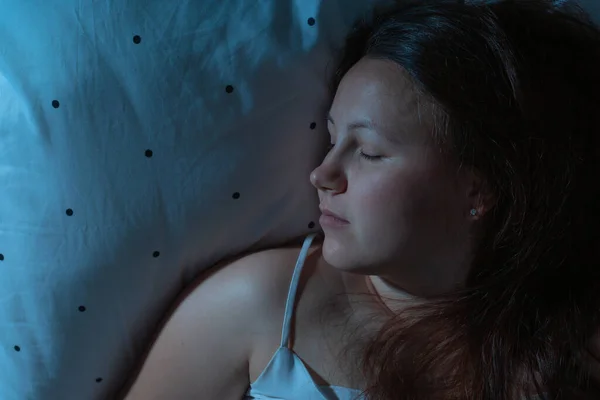 晚上躺在床上舒舒服服地睡觉的年轻女子的头像，蓝色的夜色 — 图库照片