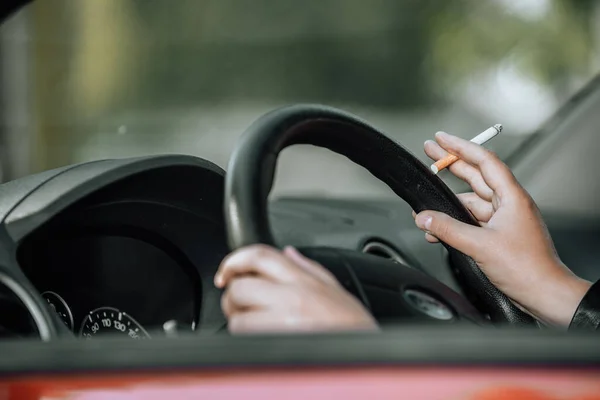 Primer plano de la mano de la mujer fumando cigarrillo dentro del coche mientras conduce un vehículo — Foto de Stock