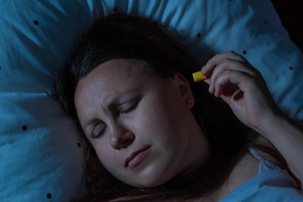 年轻女人在睡觉前把耳塞插入耳朵以减少噪音，失眠 — 图库照片