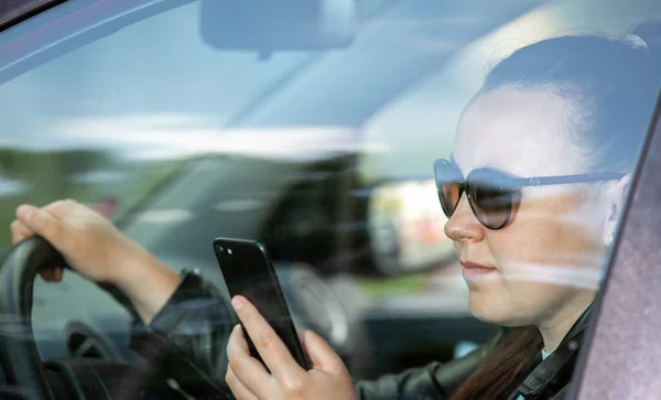 Mujer bastante joven usando un teléfono inteligente, móvil mientras conduce un coche, concepto de transporte —  Fotos de Stock