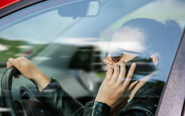 Mujer bastante joven usando un teléfono inteligente, móvil mientras conduce un coche, concepto de transporte — Foto de Stock