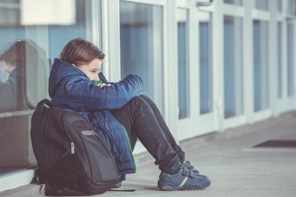 Liten pojke eller barn som sitter ensam på golvet framför skolan efter att ha utsatts för mobbning — Stockfoto