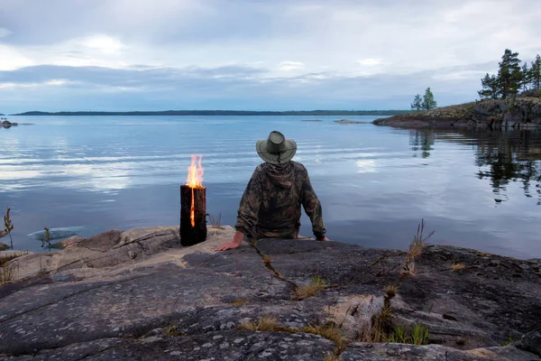Yanan Fin muma yakınındaki büyük bir kayanın üzerinde büyük bir göl kıyısında bir adam oturuyor.