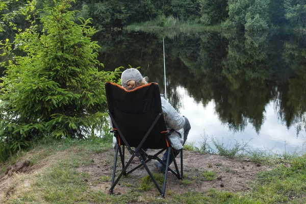 Bir kadın bir koltuk bir göl kıyısında oturuyor ve balık yakalıyor.