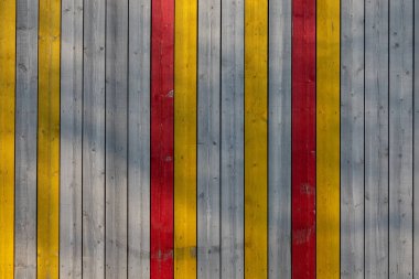 Dikey tahta duvarlar. Bazı tahtalar boyanmamış, bir kısmı sarı ve kırmızıya boyanmış. Geçmişi. Doku.