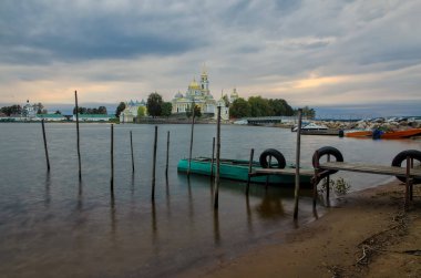 Seliger Gölü kıyısındaki erkek Ortodoks manastırı Nilova Pustyn. Akşam aydınlatması. İskelenin ön tarafında yeşil bir tekne duruyor. Direkler demirlemek için sudan çıkarlar..