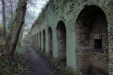 Eski kalenin iç hattı. Delikleri olan eski tuğla bir duvar küfle kaplıdır. Kış havası nem ile doludur. Duvar boyunca bir yol var. Bergues şehri. Fransa.