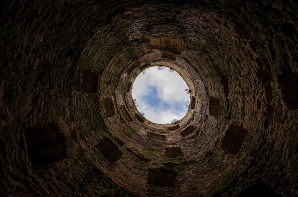 View up inside an old round fortress tower. Visible medieval brickwork and windows at different levels. In the background, a fragment of the sky with clouds is visible. Background.