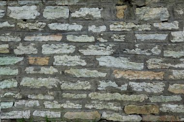 Çeşitli şekillerde doğal ışık taşlarından yapılmış bir duvar parçası. Gri bir çimento klasörü var. Sokak tasarımı. Tallinn Estonya. Geçmişi. Doku.