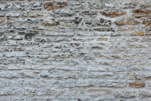 Fragment of an old fortress wall of gray and brown stones. There is a thin layer of white plaster. Tallinn Estonia. Background. Texture.