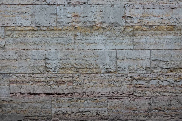 Gri taş bloklardan yapılmış binanın ön cephesinin bir parçası. Taşların yüzeyinde gözenekli bir görünüm ve yerel turuncu alanlar var. Geçmişi. Doku.