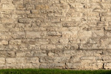 Taş bloklardan yapılmış eski bir gri kale duvarı. Aşağıda yeşil çimlerle kaplı bir arazi şeridi var. Geçmişi. Doku.