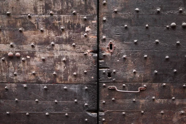 Background: fragment of a wooden door - boards painted in a  black, brown color and forged iron nails, door handle, keyhole. Style Medieval Europe (France).