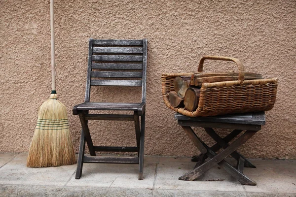 Cosas vintage: viejo jardín francés silla de madera y taburete plegable y cesta de mimbre con leña para la chimenea o estufa y escoba. fondo - paredes de color rosa amarillo. Provenza. Francia . — Foto de Stock