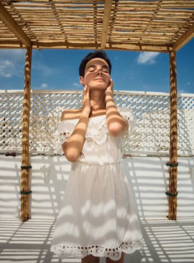 Terasta beyaz elbiseli bir kız. Gölgede yüz. Çizgili gölge. Dinlenmek, tatil, seyahat. Tunus.