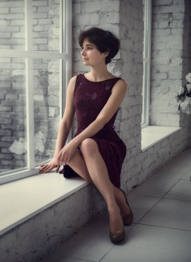 Elbiseli kıza pencerenin kenarında oturur. Mesafe içine bakıyor.