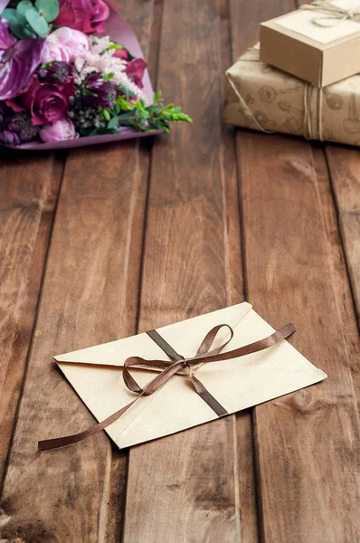 Vacker handgjord presentask (paket) med blommor bukett, kuvert med Tom gåva tag och dekorativa rep på trä bakgrund — Stockfoto