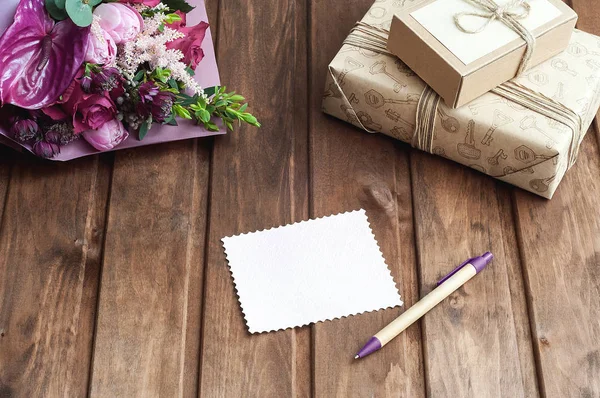 Caixa de presente artesanal bonita (pacote) com buquê de flores, envelope com etiqueta de presente em branco e corda decorativa no fundo de madeira — Fotografia de Stock