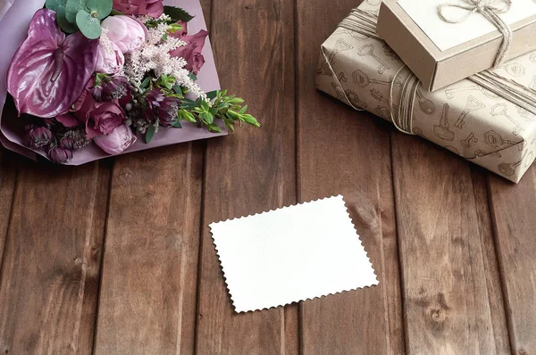 Caixa de presente artesanal bonita (pacote) com buquê de flores, envelope com etiqueta de presente em branco e corda decorativa no fundo de madeira — Fotografia de Stock