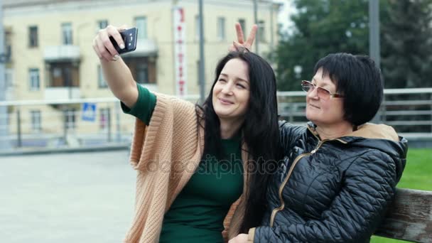 Mamá e hija se están divirtiendo juntas mientras hacen selfies en un teléfono inteligente. Una mujer adulta representa cuernos en una joven . — Vídeo de stock