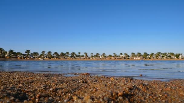 Praia de areia com pequenos seixos no resort. Belo céu azul. Pequenas ondas rolam lentamente até a costa . — Vídeo de Stock