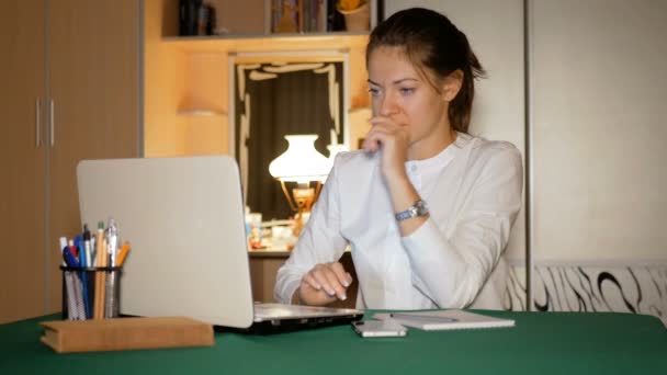 Meisje gekleed in een witte blouse is thuis werken achter een laptop. Journalist ziet er op het scherm en is erg nerveus dat ze er niet in slaagt. — Stockvideo