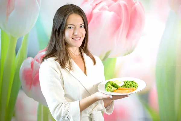Genç bir kadın bir tabak haşlanmış sebze tutuyor. Doğru beslenme propaganda.